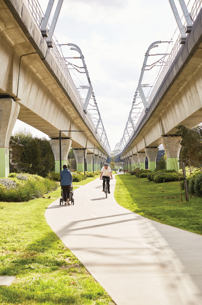 Man on a riding a bike along a path and person pushing a parm