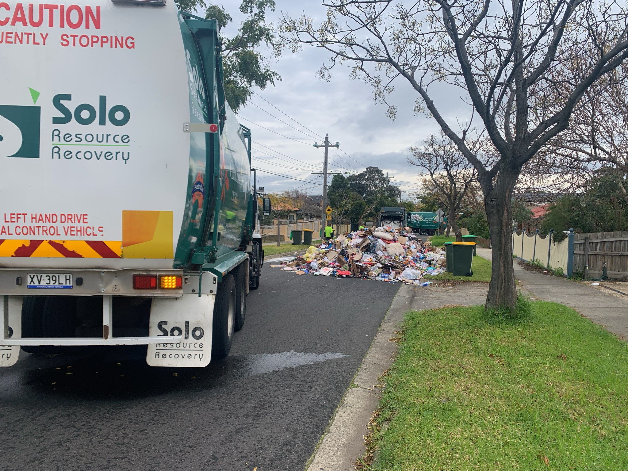 Solo Resource Recovery trucks collect a large pile of uncontained household rubbish left on a suburban street.