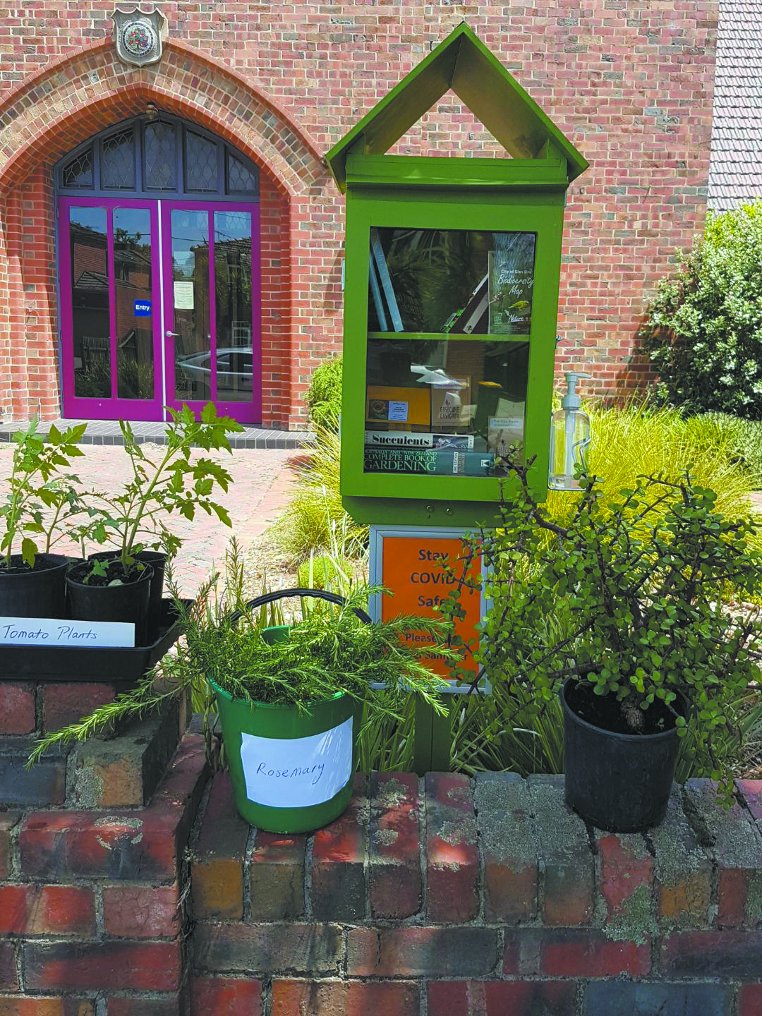 Books in a green glass-doored street library and free plants