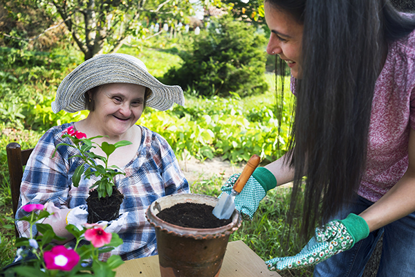 Women with down sybdrome and her friend planting flowers in a pot.