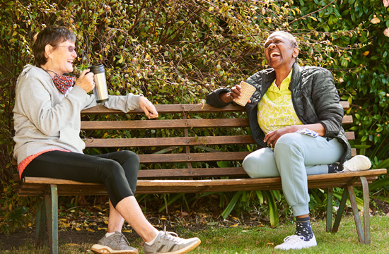 Friends sitting on a park bench talking and laughing.