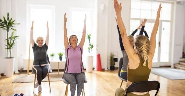 Participants take part in a chair yoga class, performing seated stretches with their arms raised overhead.