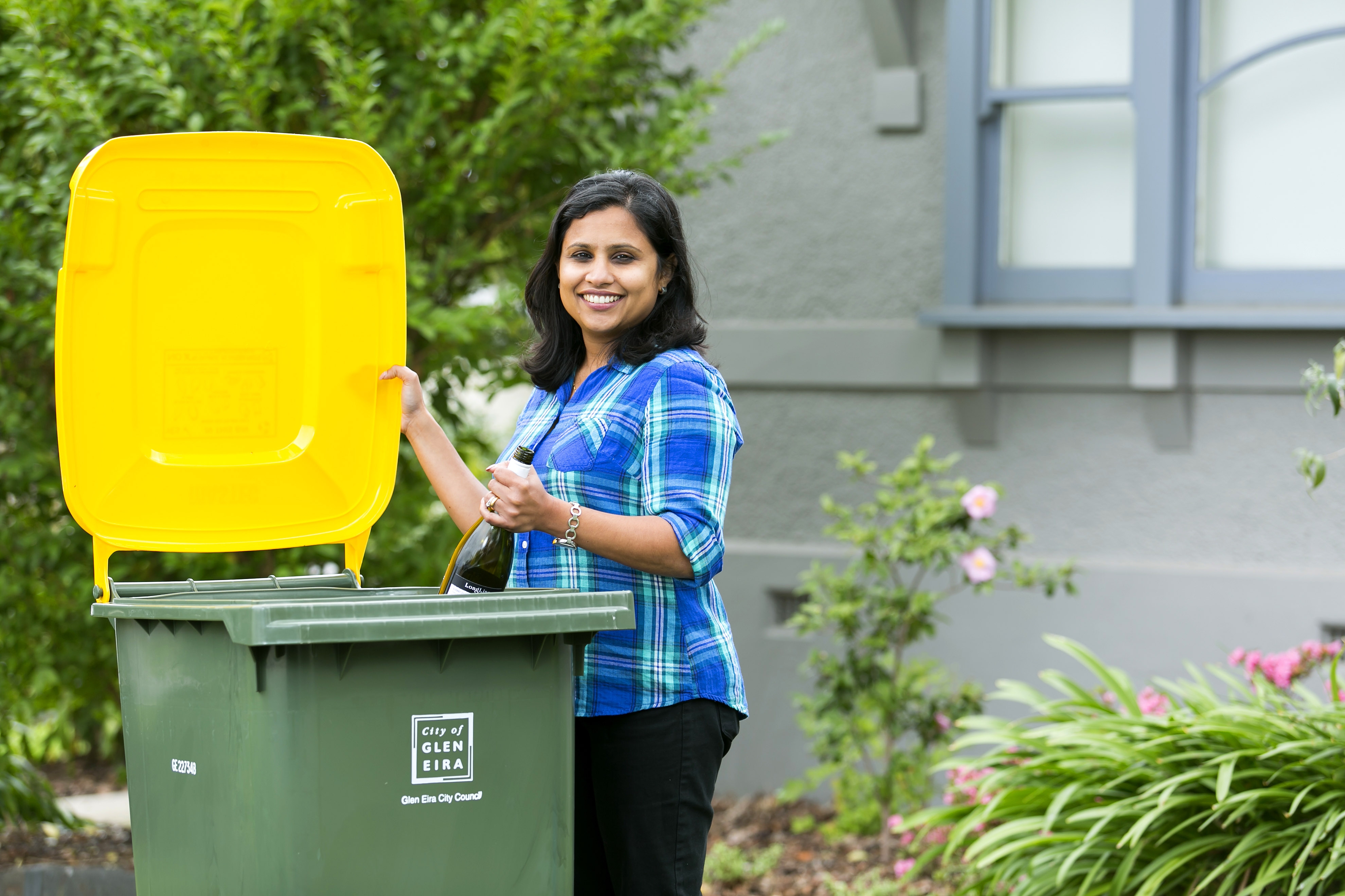 Woman in blue shirt recycling a wine bottle in her yellow-lidded recycling bin