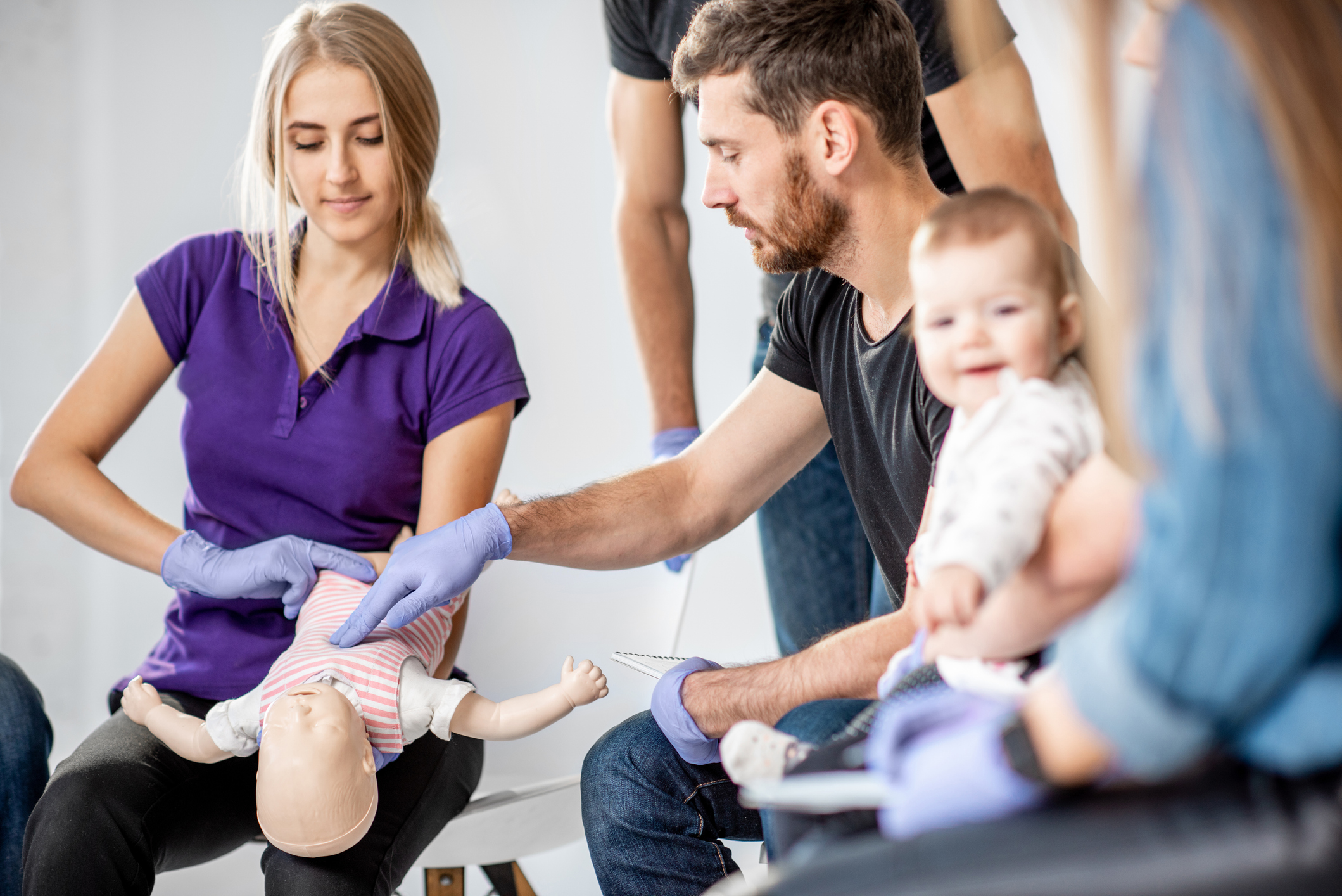 Participants practise infant first aid techniques on a baby mannequin during a hands-on first aid training session.