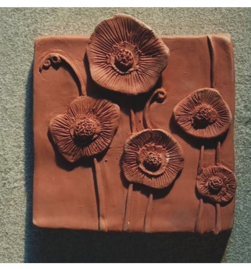Clay relief artwork featuring textured flowers sculpted from clay on a square tile during a clay sculpting workshop.