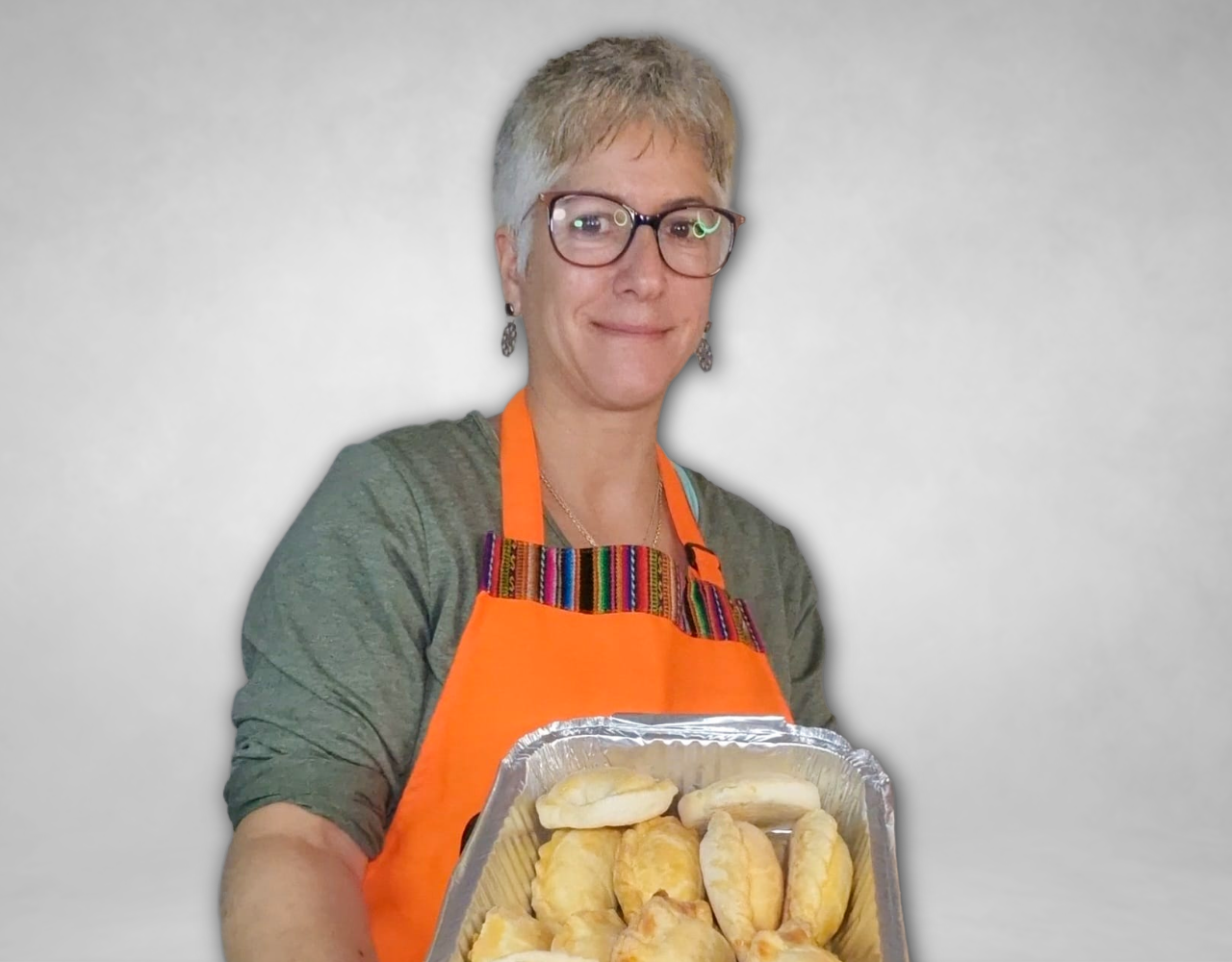 Person wearing an orange apron holding a tray of baked pastries against a plain grey background.