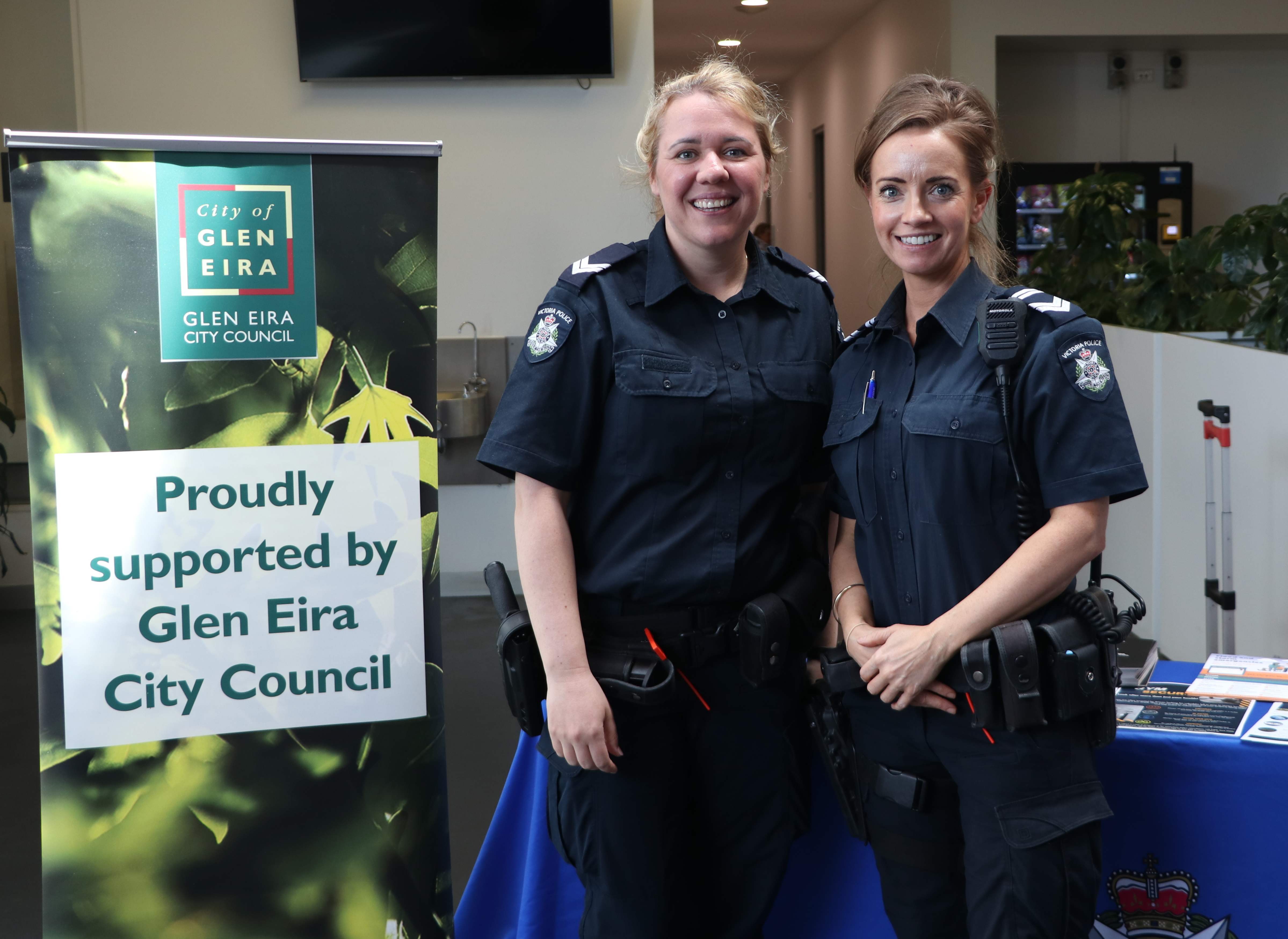 Two Victoria Police officers stand beside a Glen Eira City Council display banner at a community event.