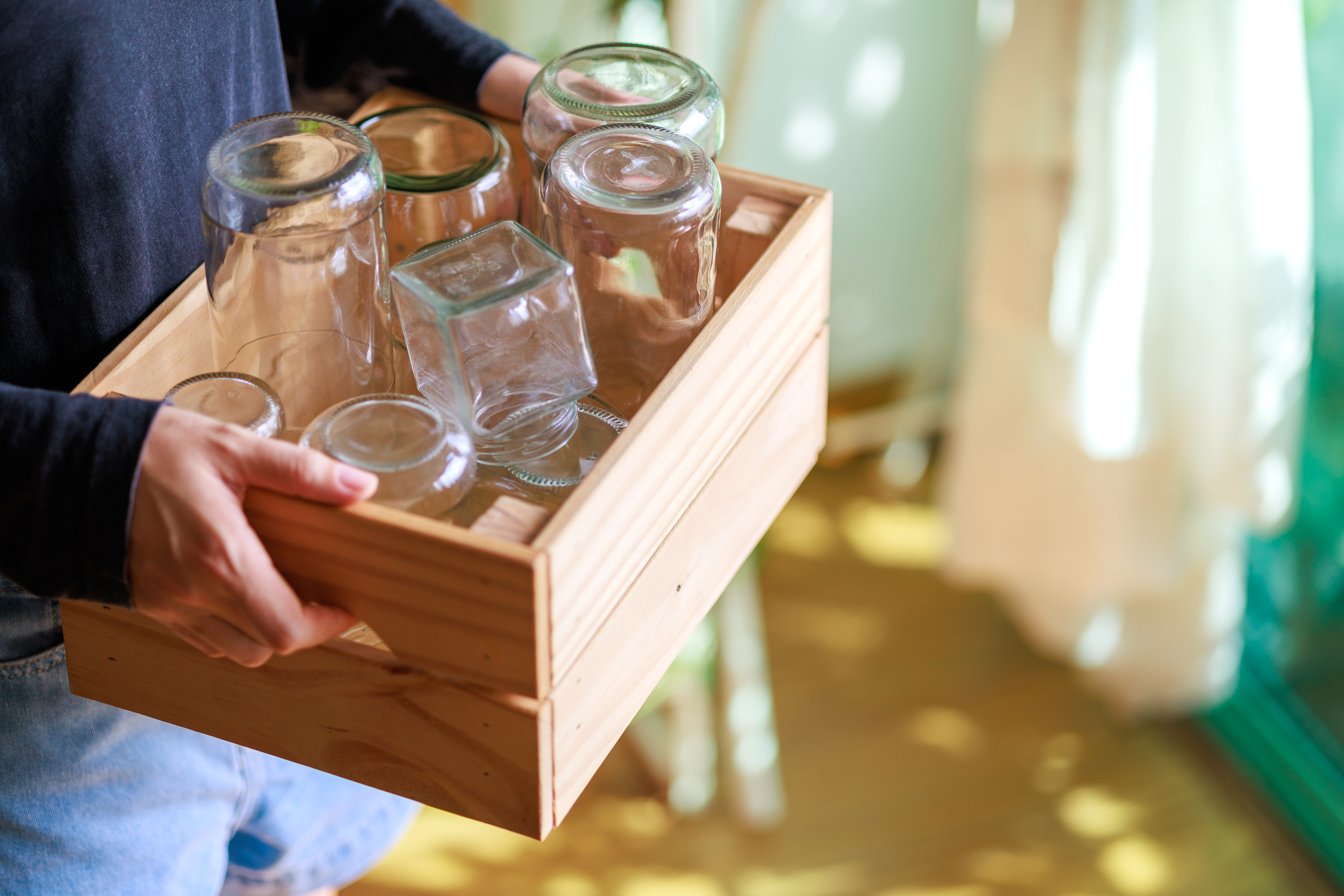 A person carries a crate of clean glass jars, highlighting recycling, reusing and reducing household waste.