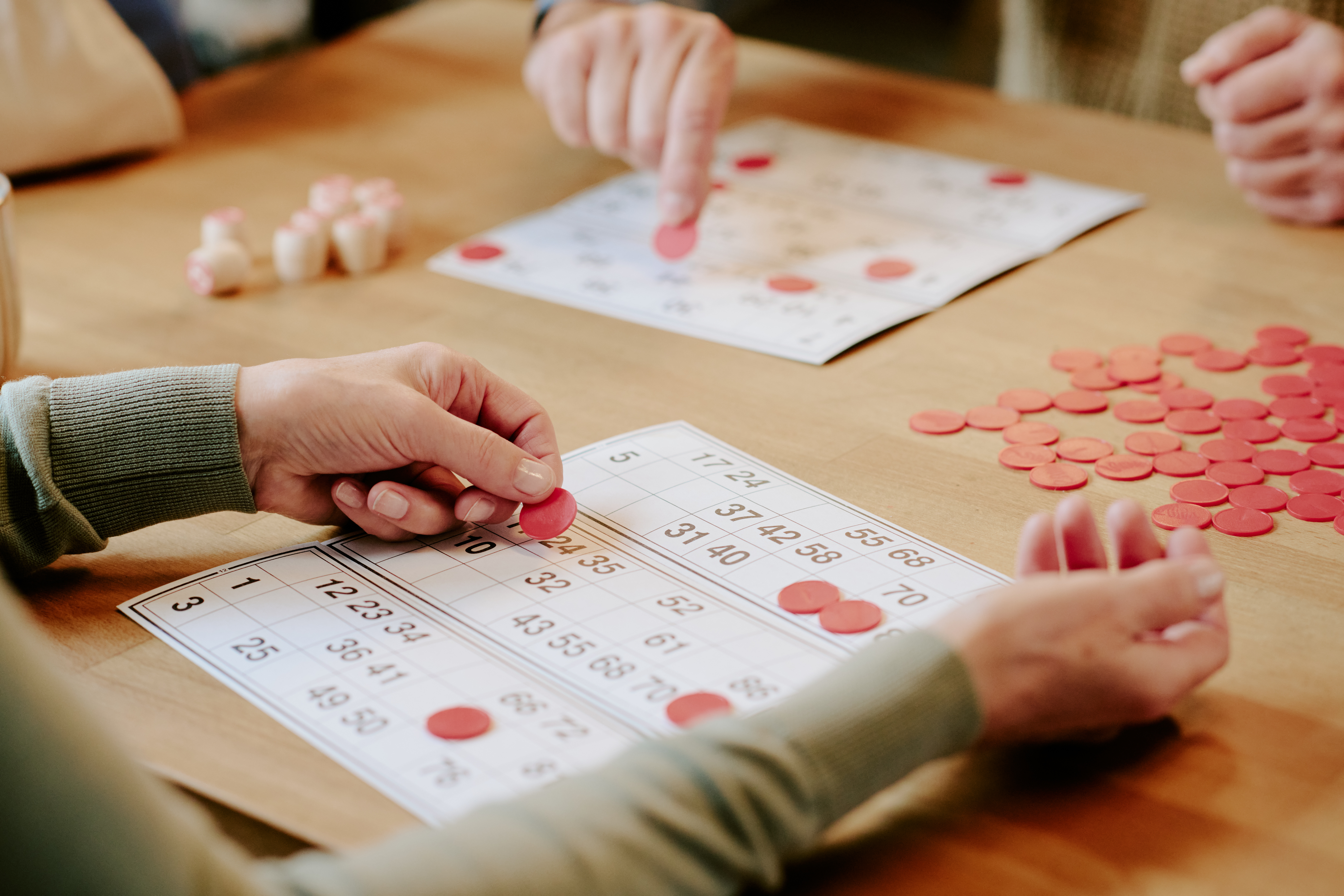 People play bingo around a table, placing counters on numbered bingo cards during a social games session.