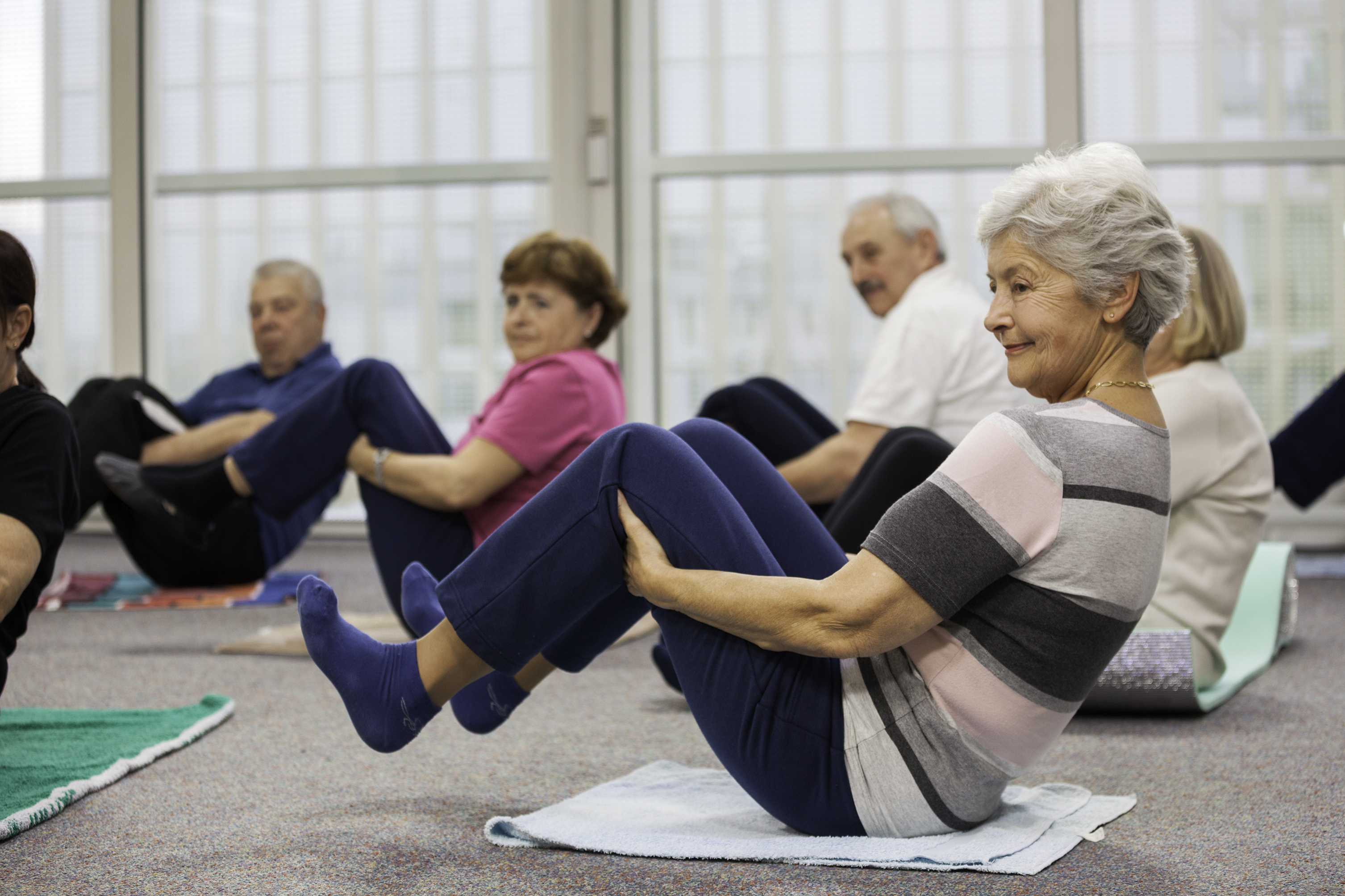Older adults take part in a strength and fitness class, performing guided floor exercises in a community setting.