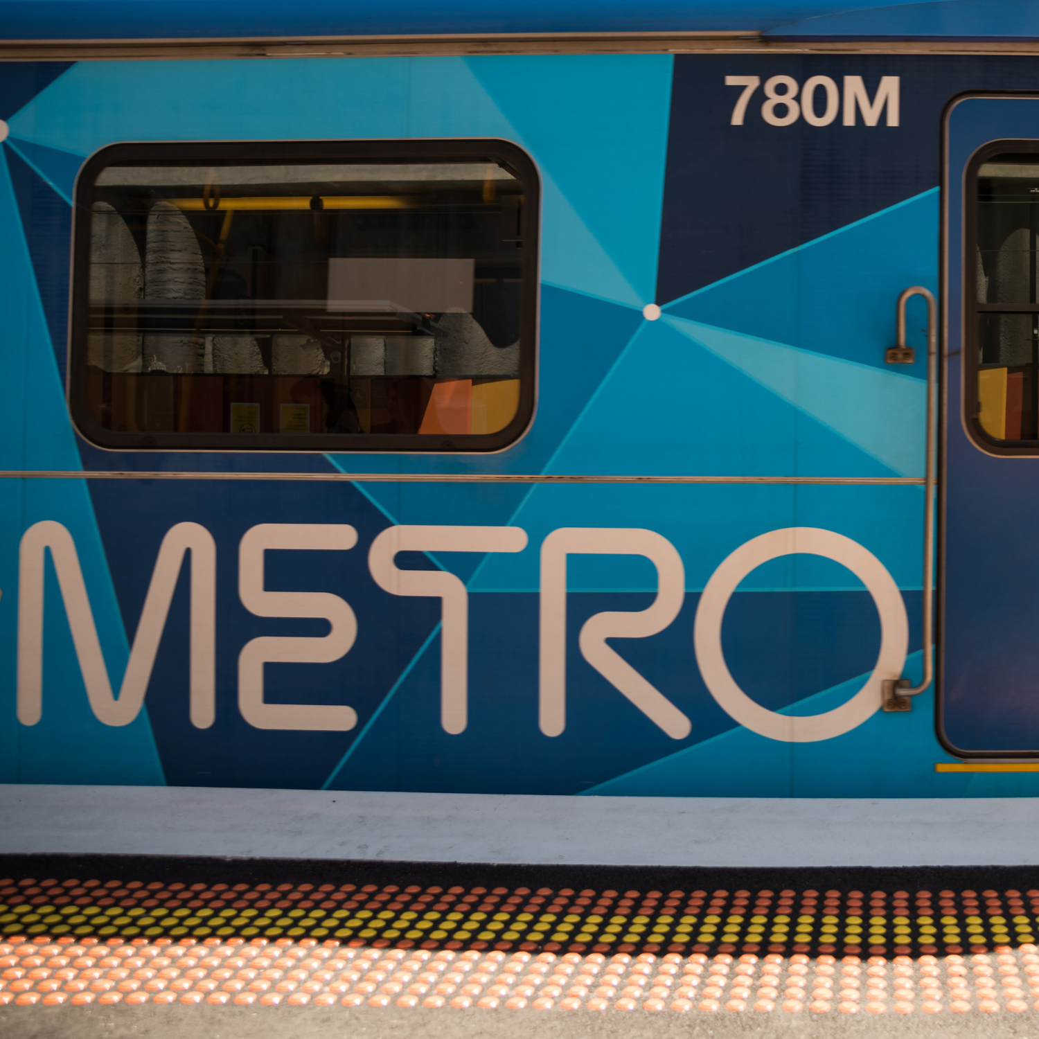 Metro train at a station platform featuring a blue geometric design and Metro branding.