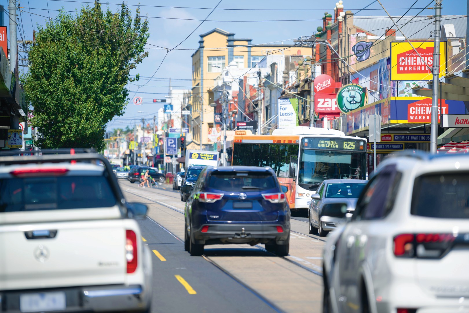 Busy streetscape in Carnegie activity centre with cars, a tram and local shopfronts along a vibrant shopping strip.