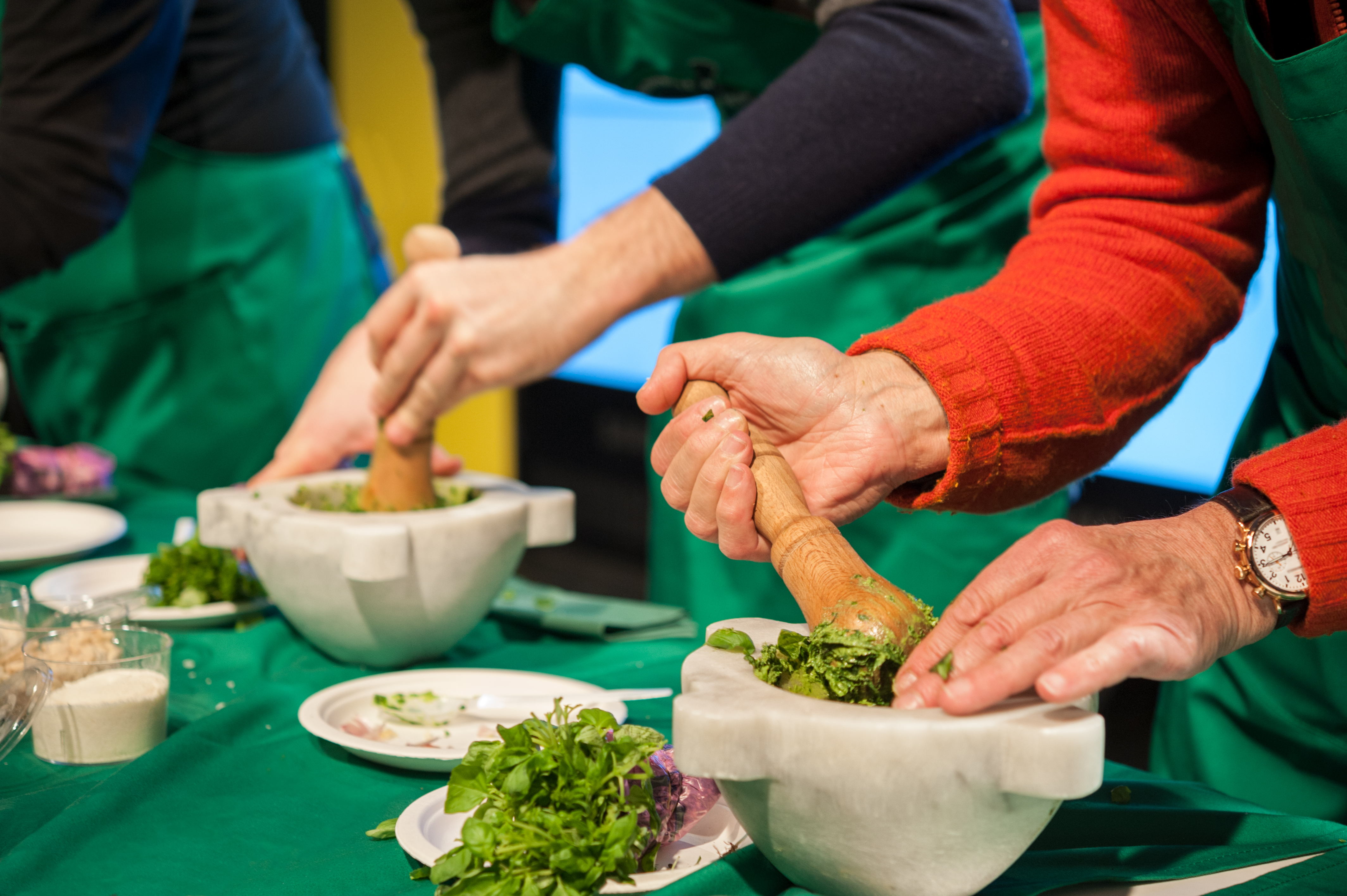 Participants make fresh pesto using a mortar and pestle during a hands-on cooking class.