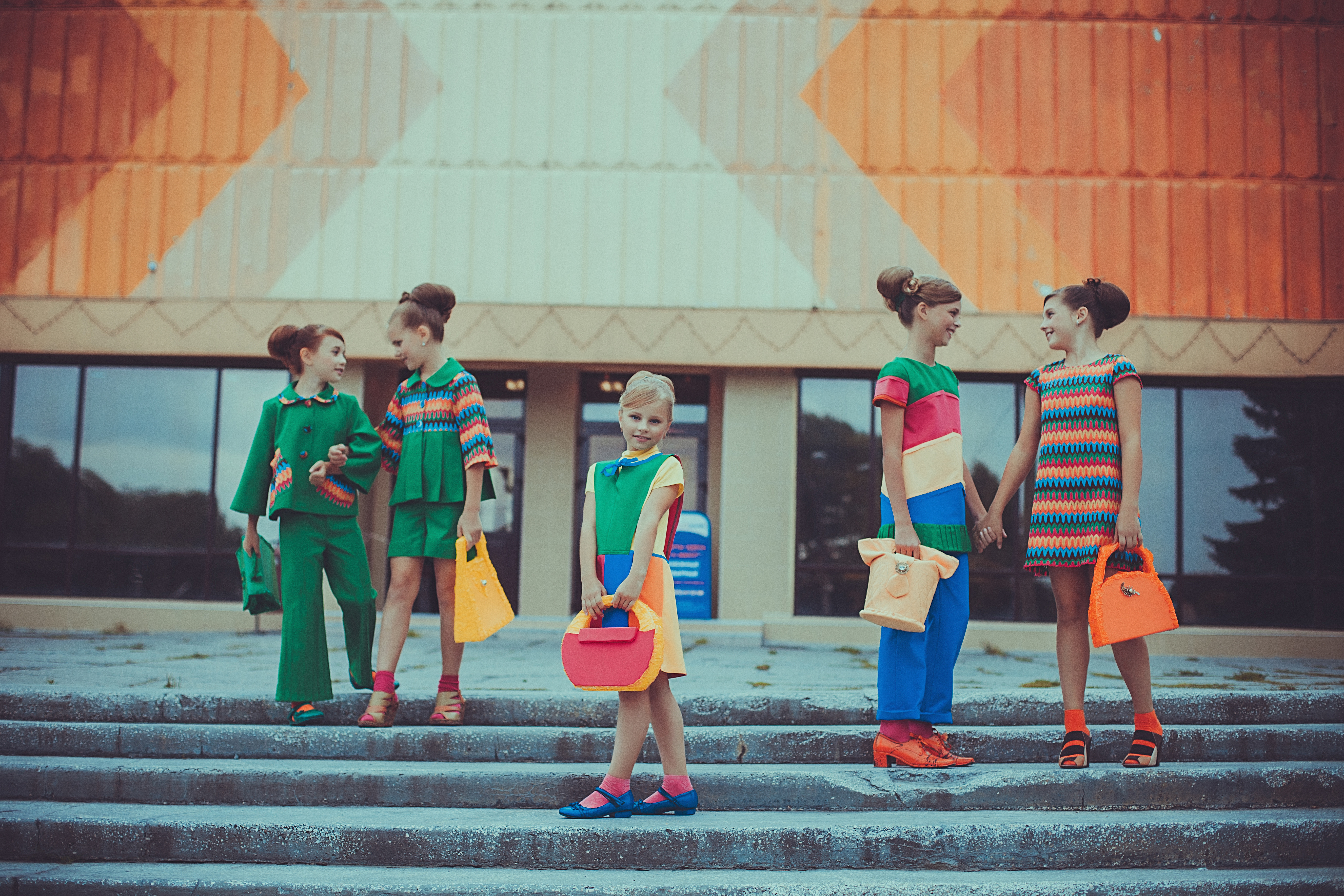 Children model colourful handmade outfits and accessories while standing on outdoor steps in front of a building.