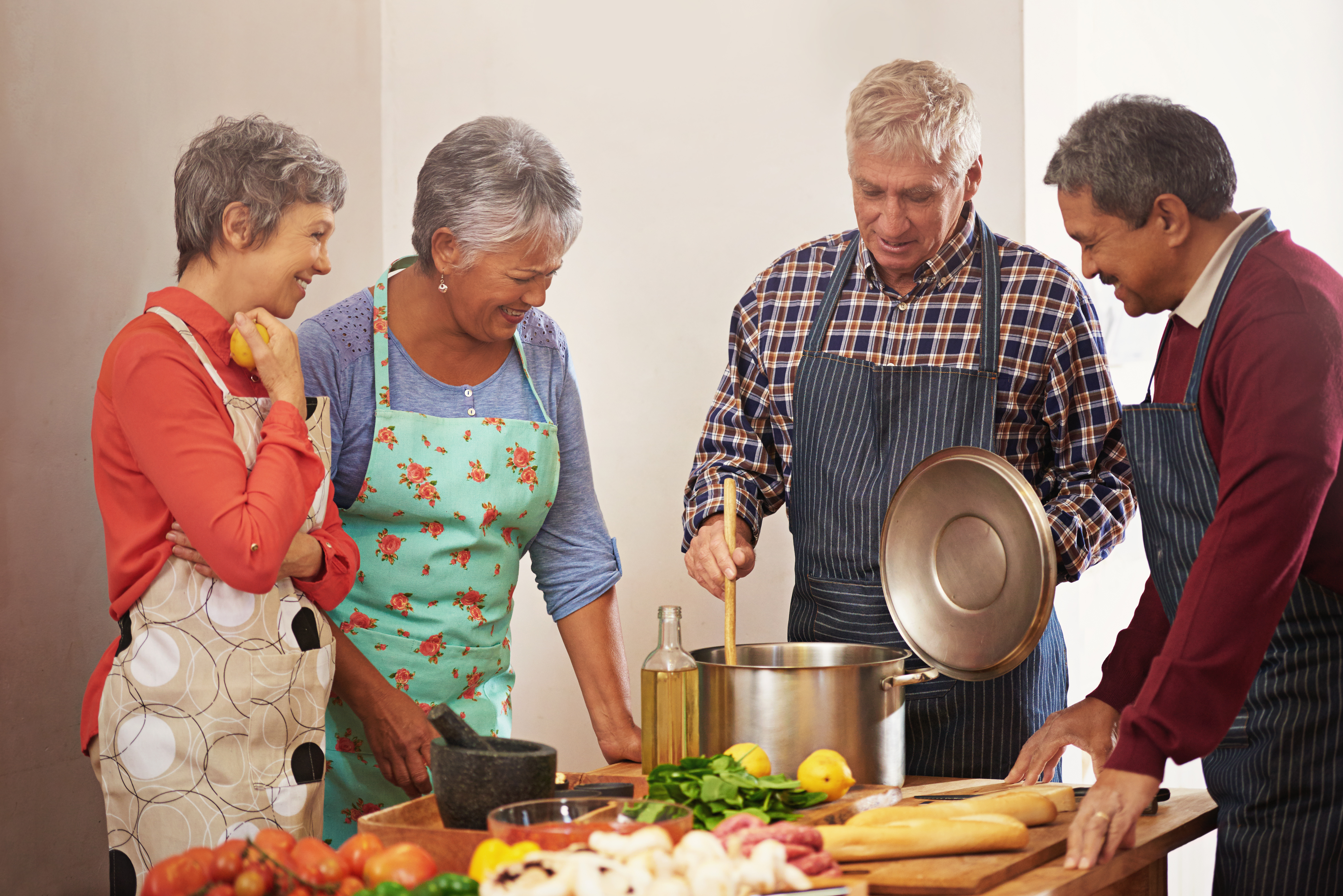 Participants prepare a shared meal together in a cooking class, standing around a kitchen bench with fresh ingredients and cookware.
