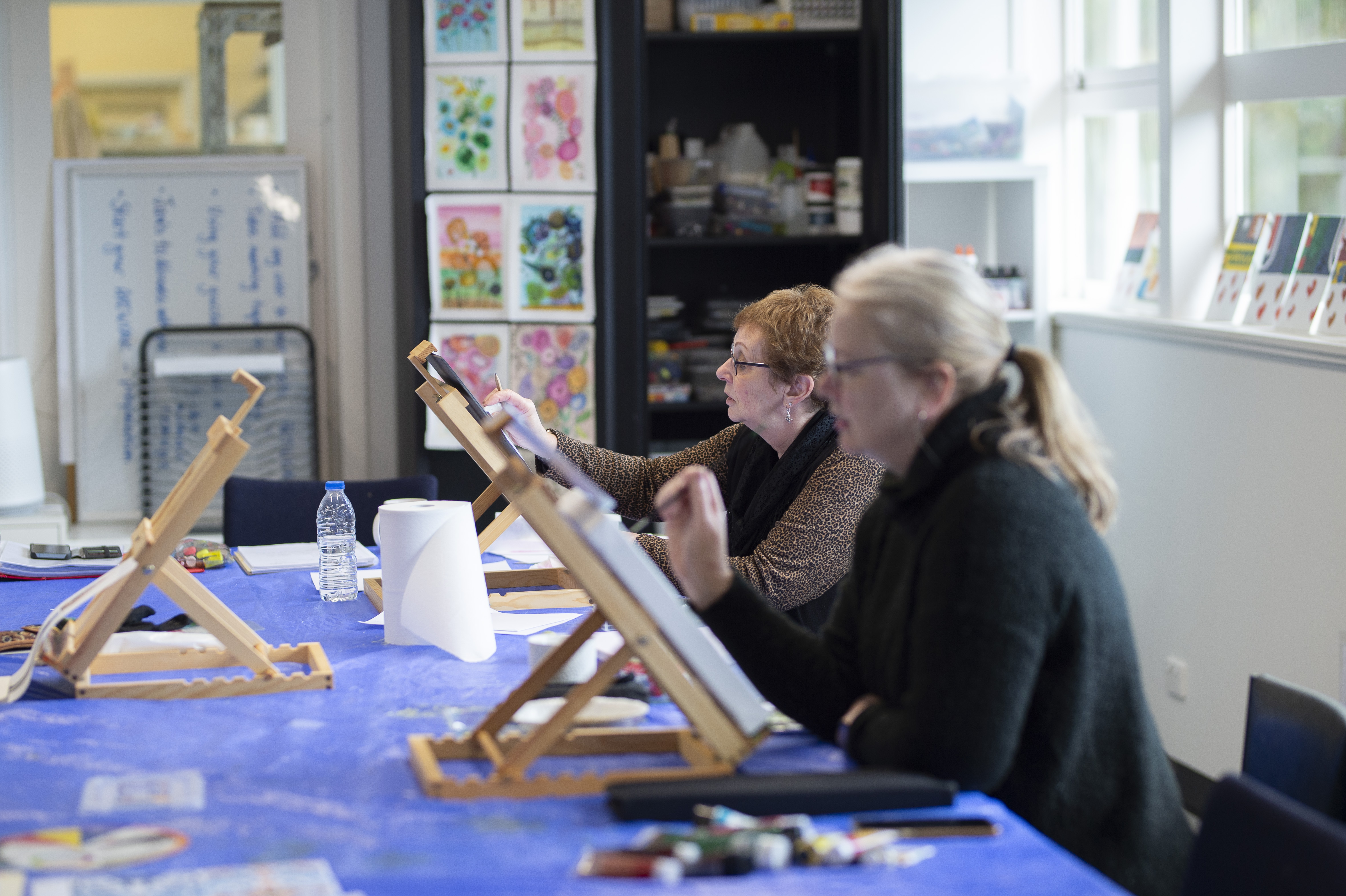 Participants paint at easels during an acrylic painting class in a community art studio.
