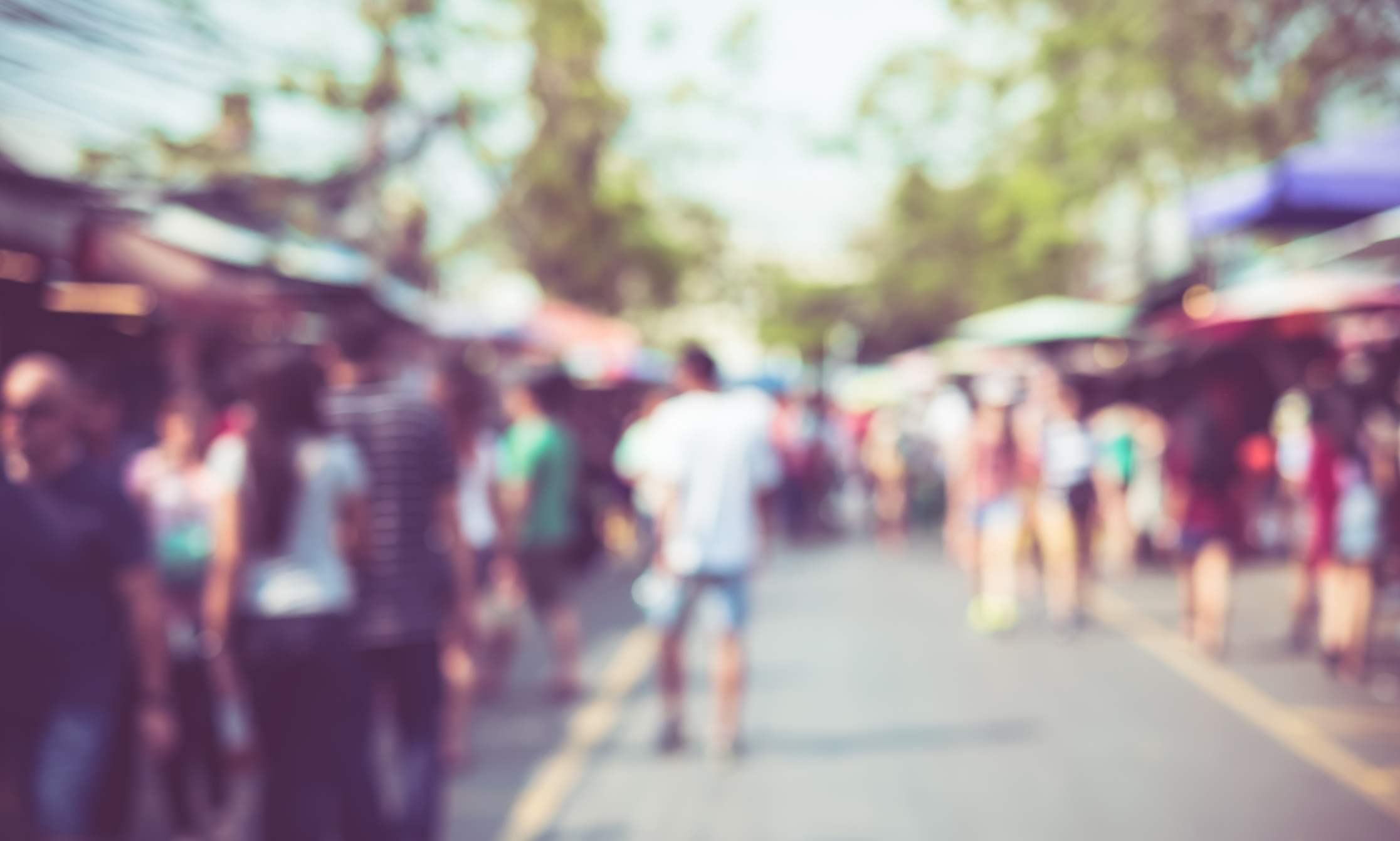 People walking between colourful stalls at an outdoor community event.